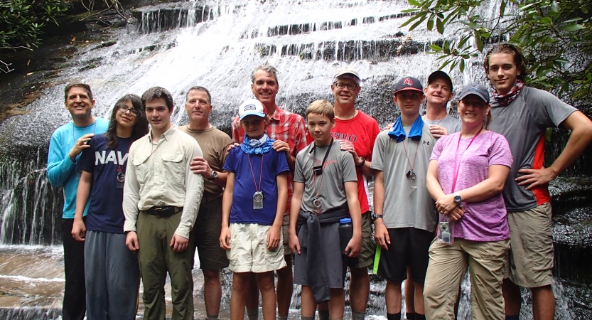 A group of parents and children pose for a group photo in front of a waterfall.